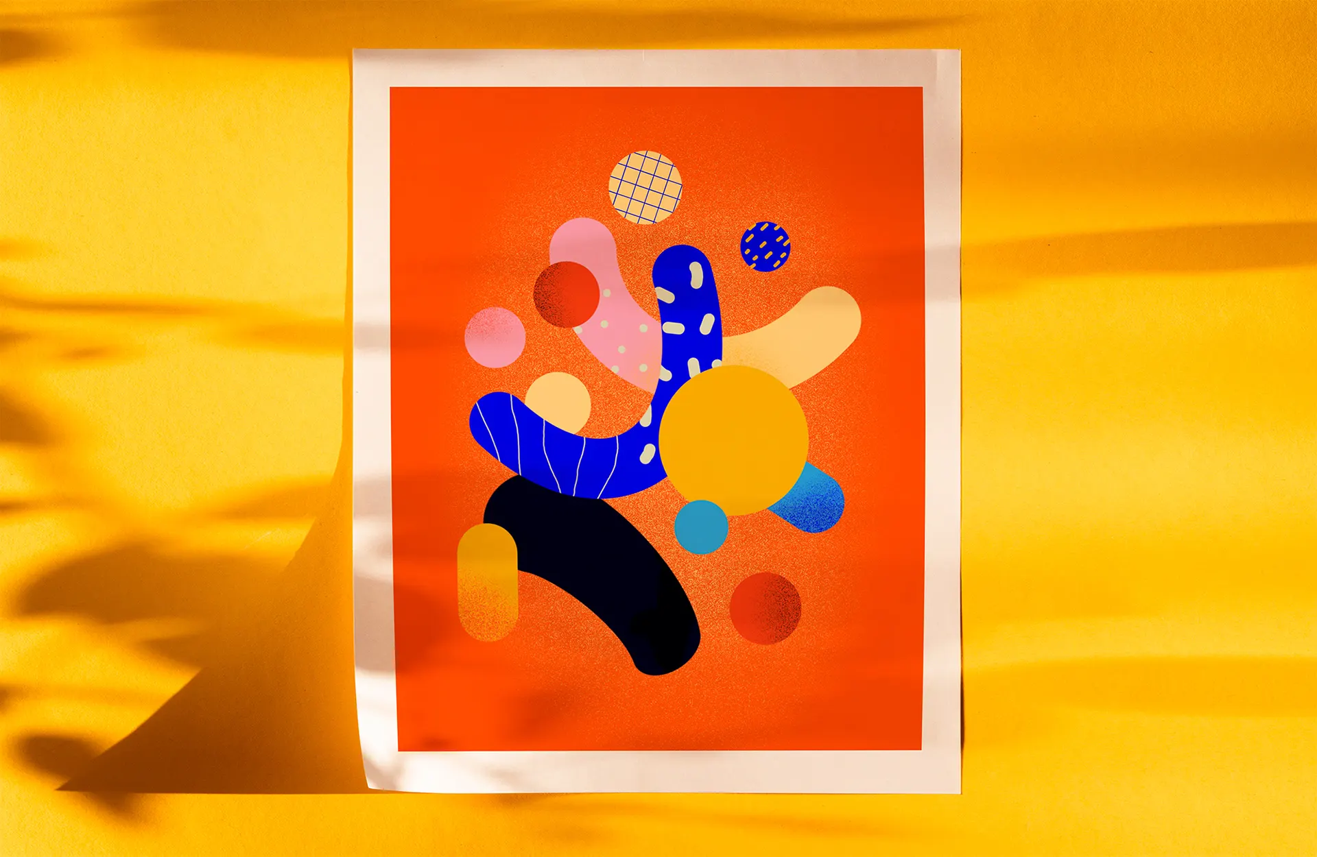 Print of an abstract composition of shapes on orange, leaning against a sunlit yellow wall