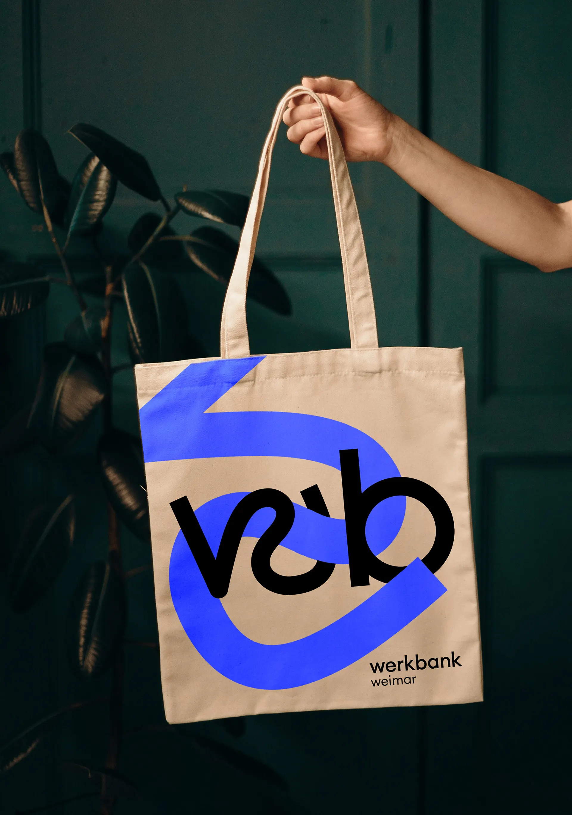 Tote bag with the Werkbank monogram in front of a dark green wall