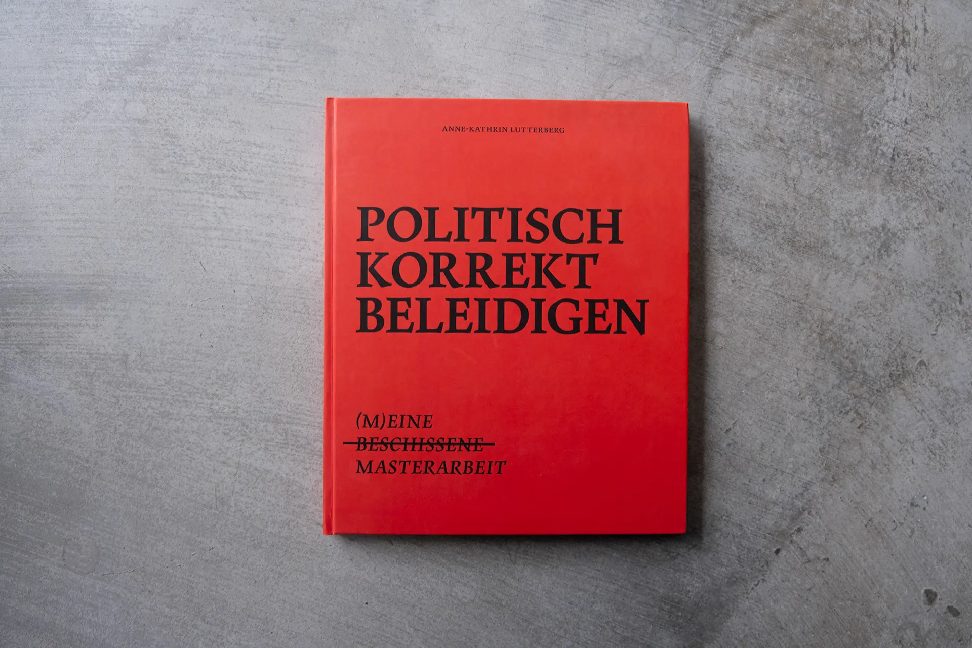 Red book cover titled “Politisch korrekt beleidigen” on grey concrete