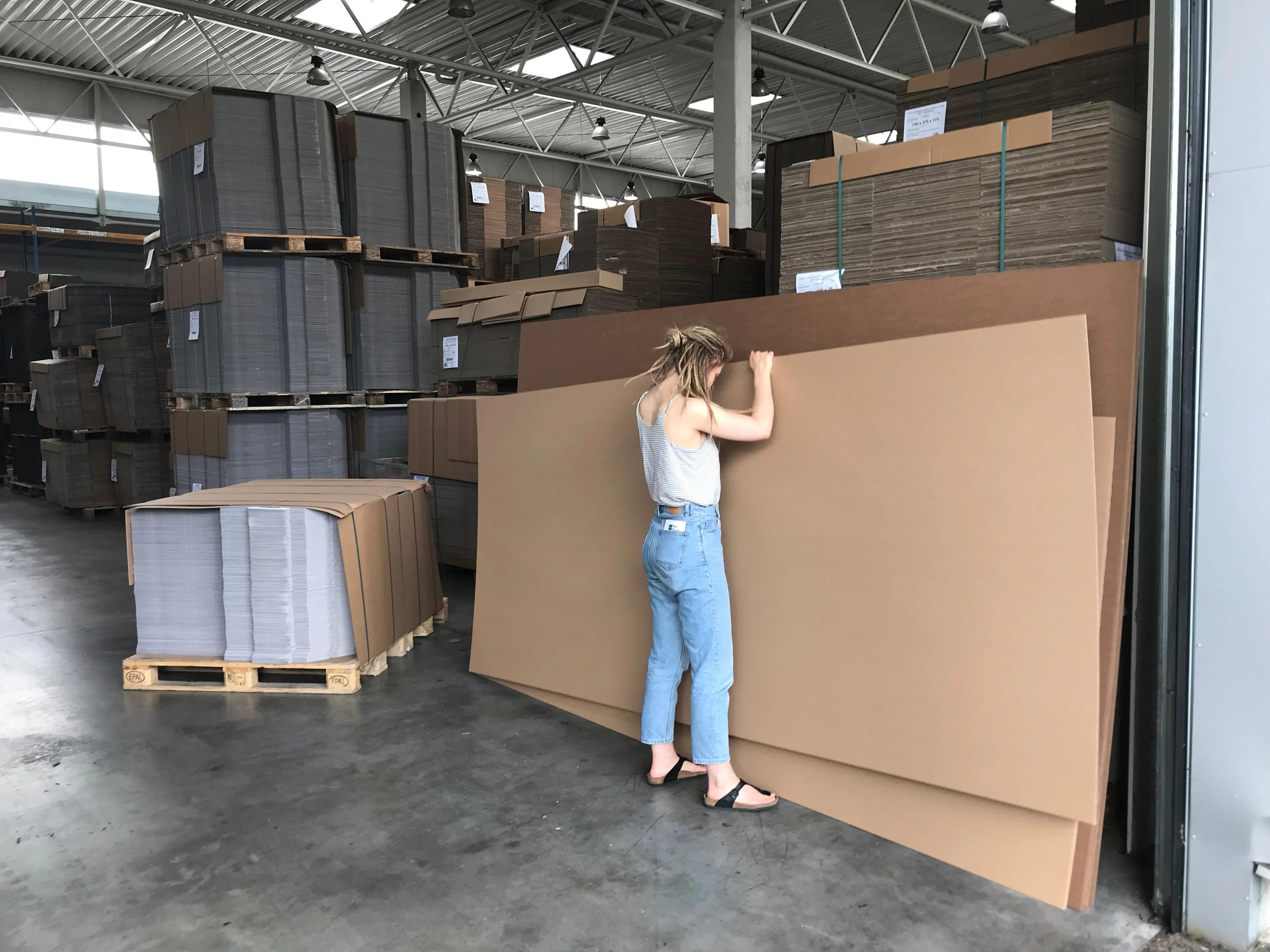 A person stands in front of large sheets of cardboard in a warehouse – model building for the wave