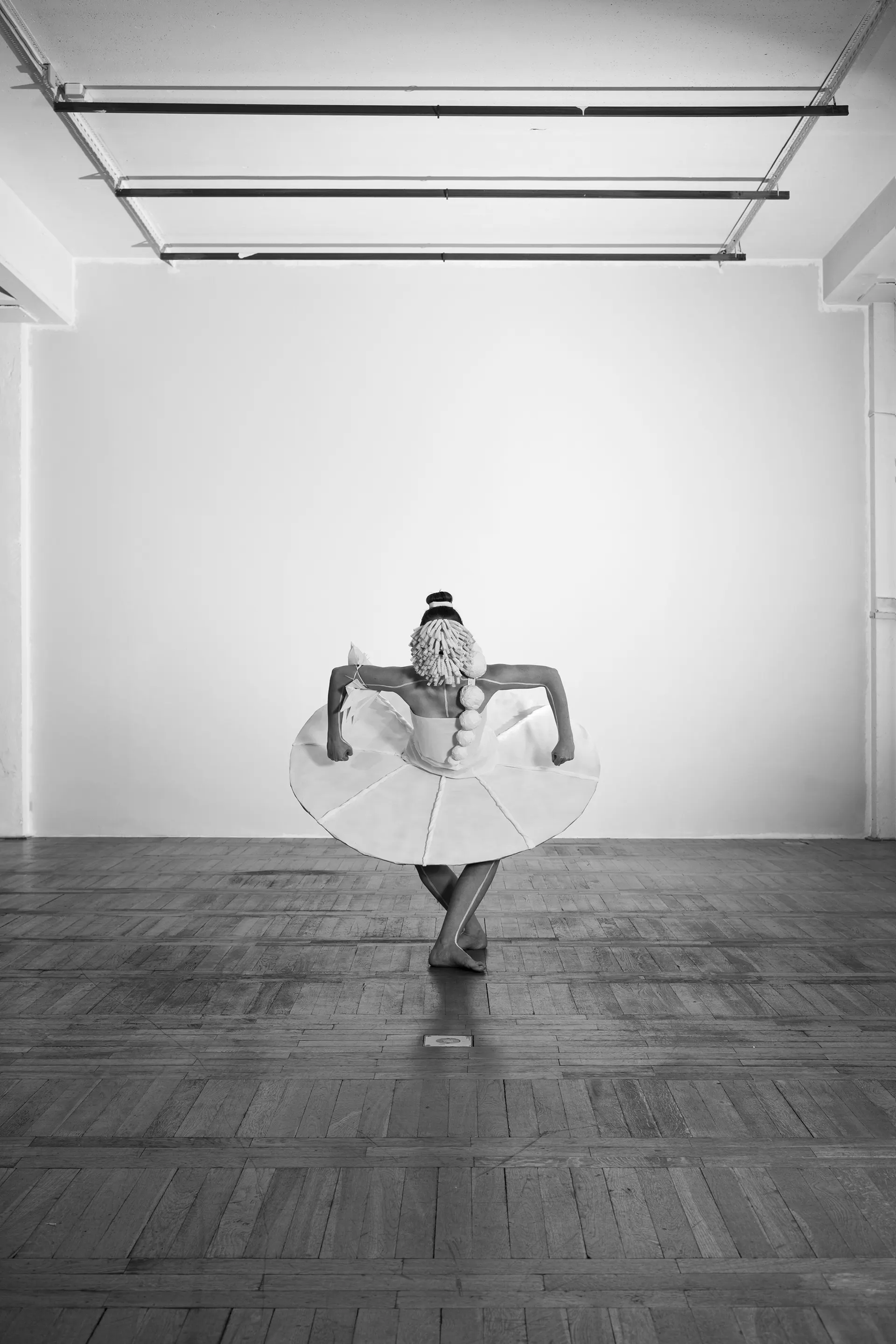 Dancer in the paper costume bowing with crossed legs, black and white