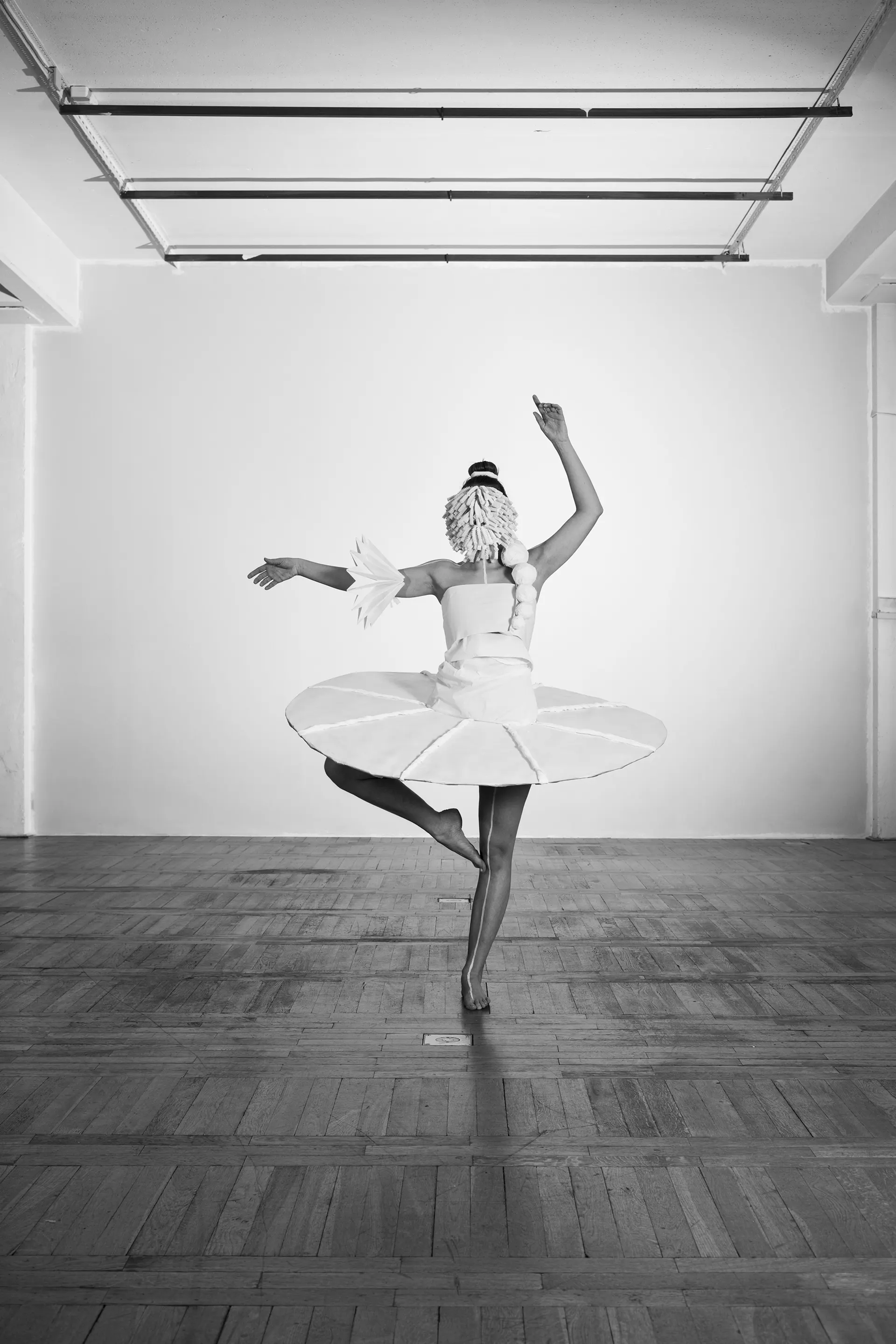 Dancer on one leg with outstretched arms in the paper costume, black and white