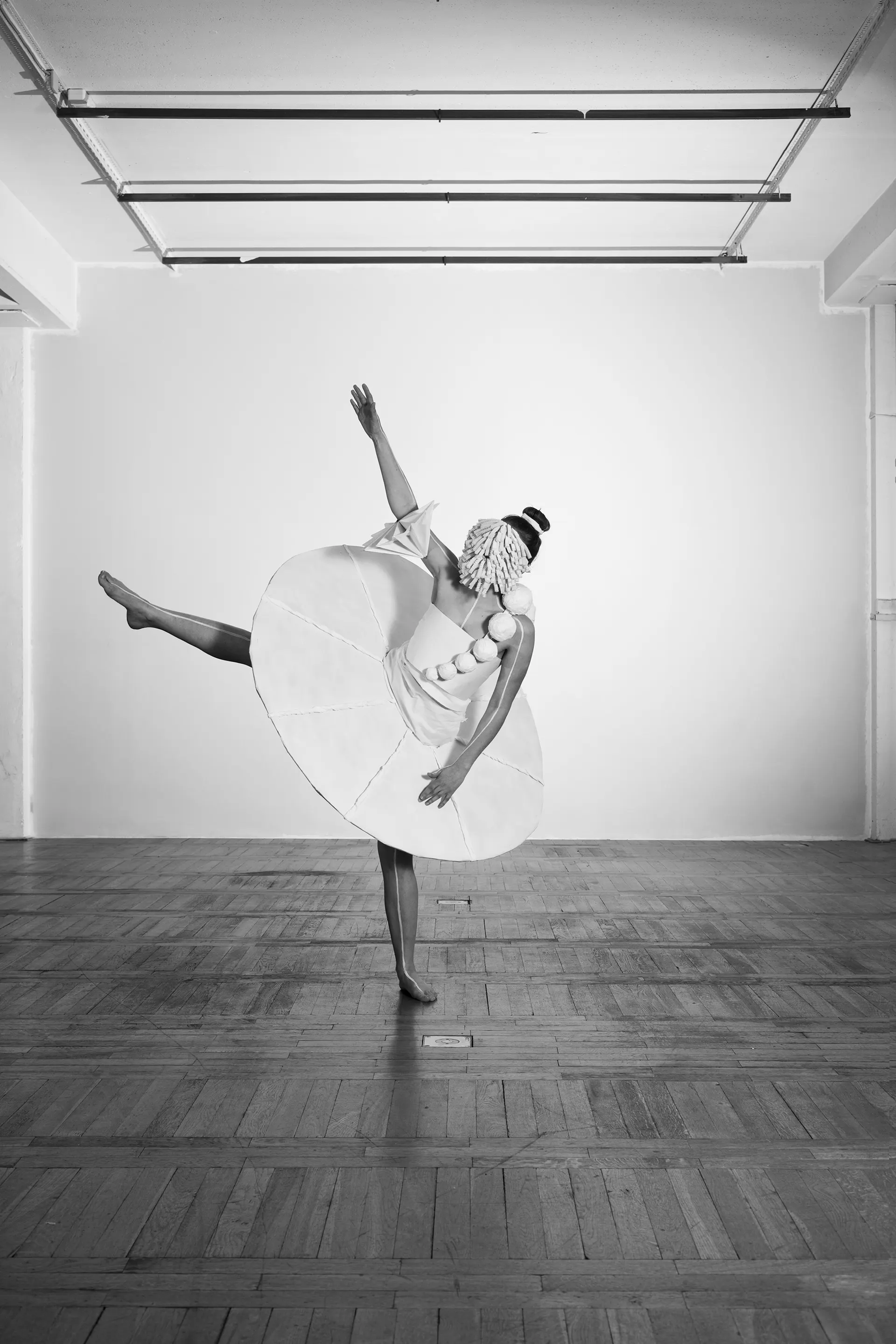 Dancer with one leg raised high, the paper skirt forming a disc in space, black and white