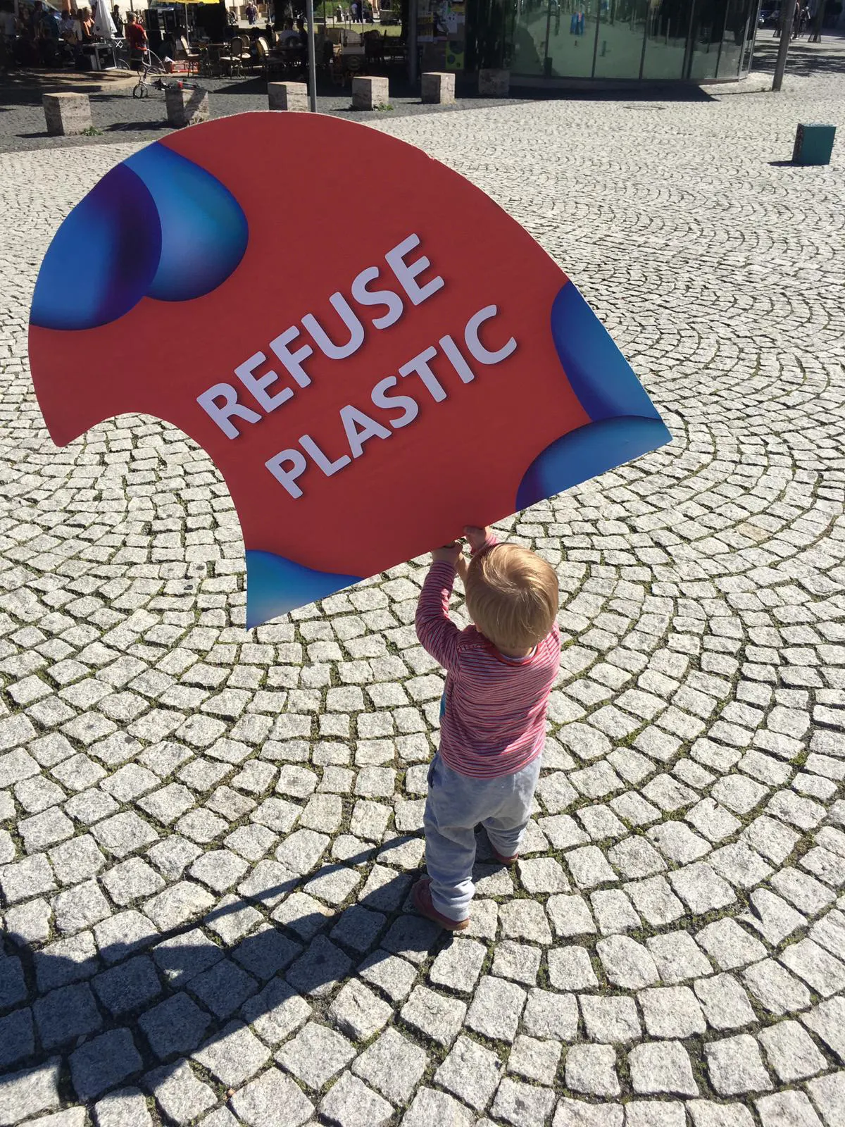 A child carrying a wave-shaped sign reading “Refuse Plastic”