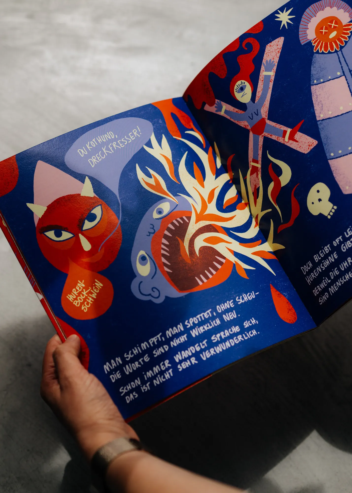 Hands holding a blue spread with a devil figure and flames