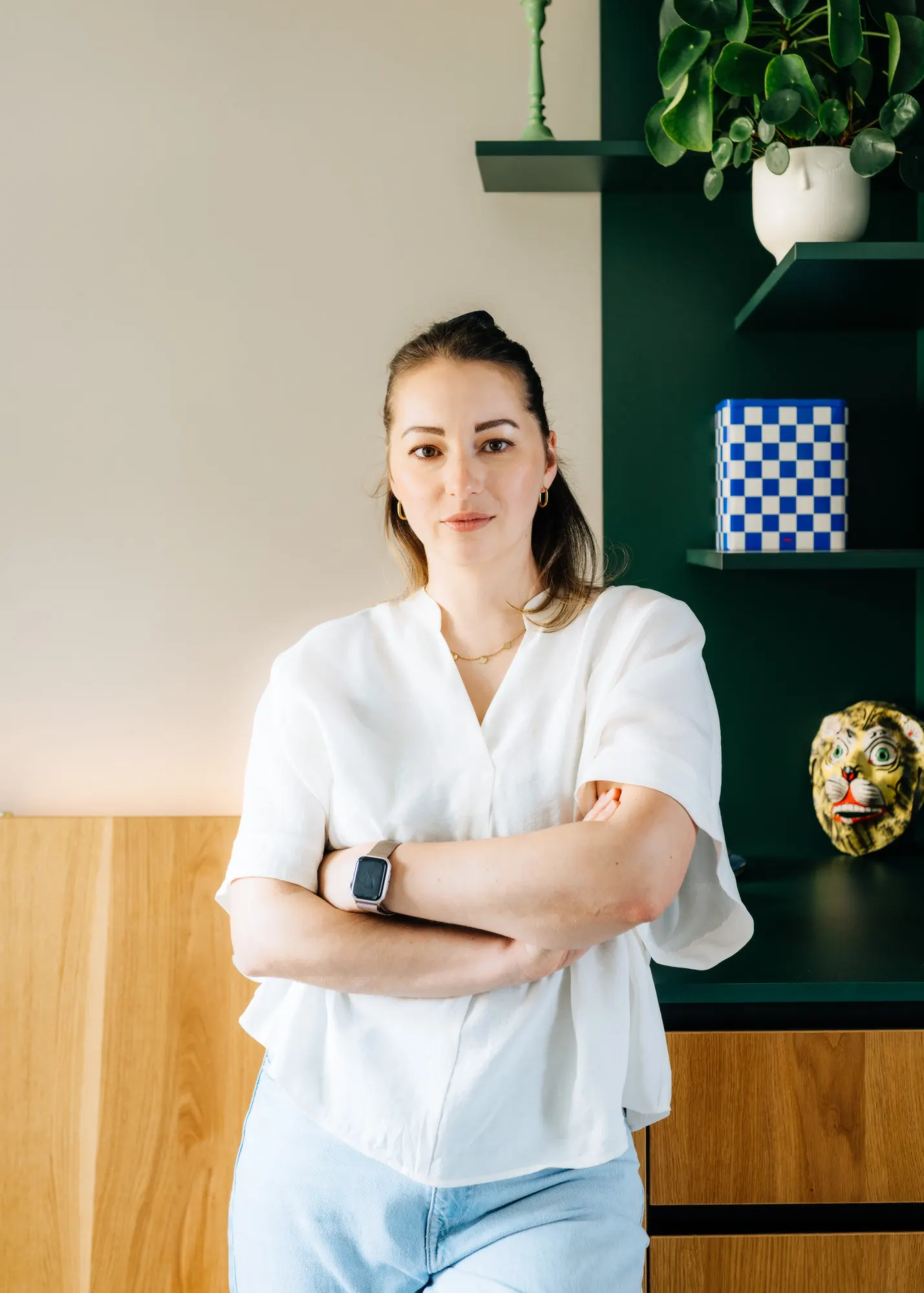 Anne Lutterberg with arms crossed in front of a dark green shelf with plants
